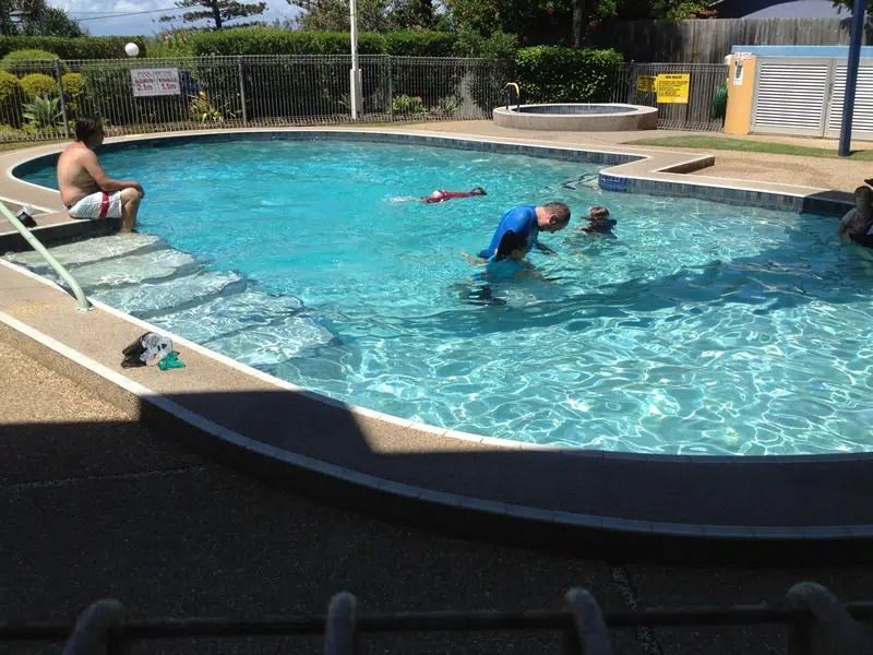 People Swimming in an Outdoor Pool on a Sunny Day — Mad Pool Interiors and Renovations in Baringa, QLD