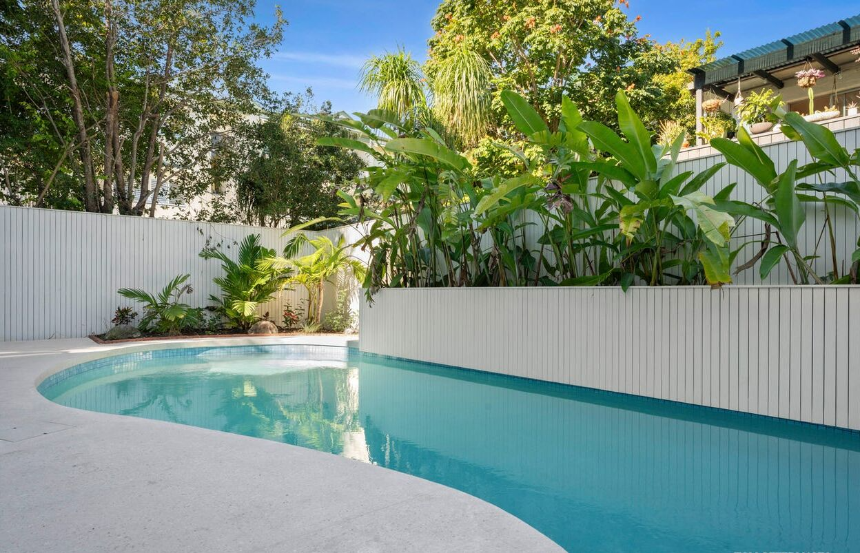 Curved Backyard Swimming Pool Beside a White Fence — Mad Pool Interiors and Renovations in Baringa, QLD