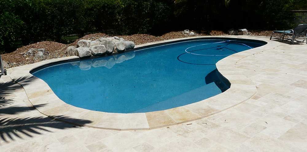 Blue Swimming Pool With Concrete Deck and Rocks Along the Edge — Mad Pool Interiors and Renovations in Baringa, QLD