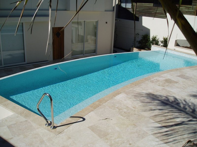 Pool With Light Blue Water and Stone Patio Next to a White Building — Mad Pool Interiors and Renovations in Baringa, QLD