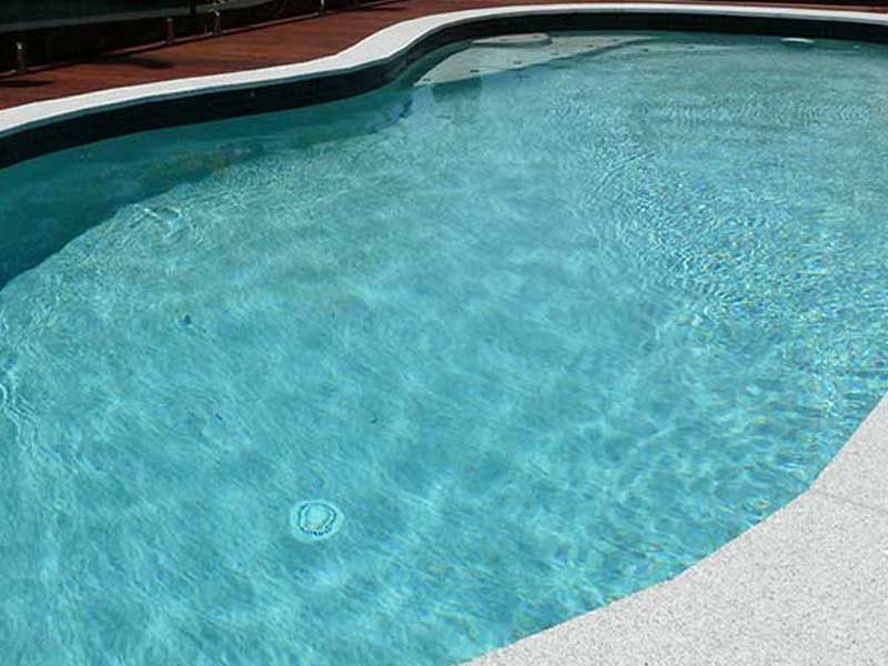 Blue Swimming Pool With White Border and Wooden Deck — Mad Pool Interiors and Renovations in Baringa, QLD