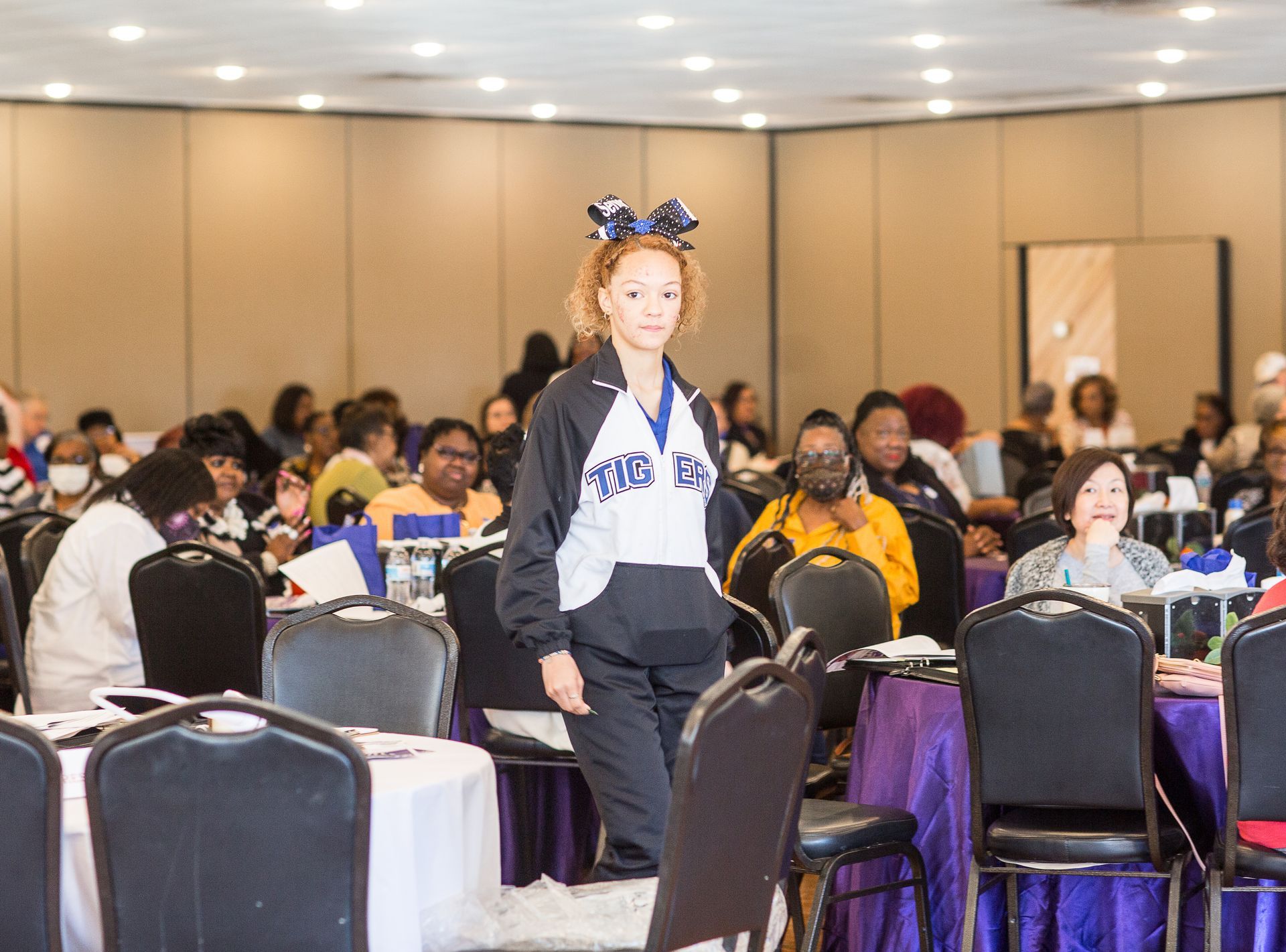 A cheerleader is walking in a room with tables and chairs.