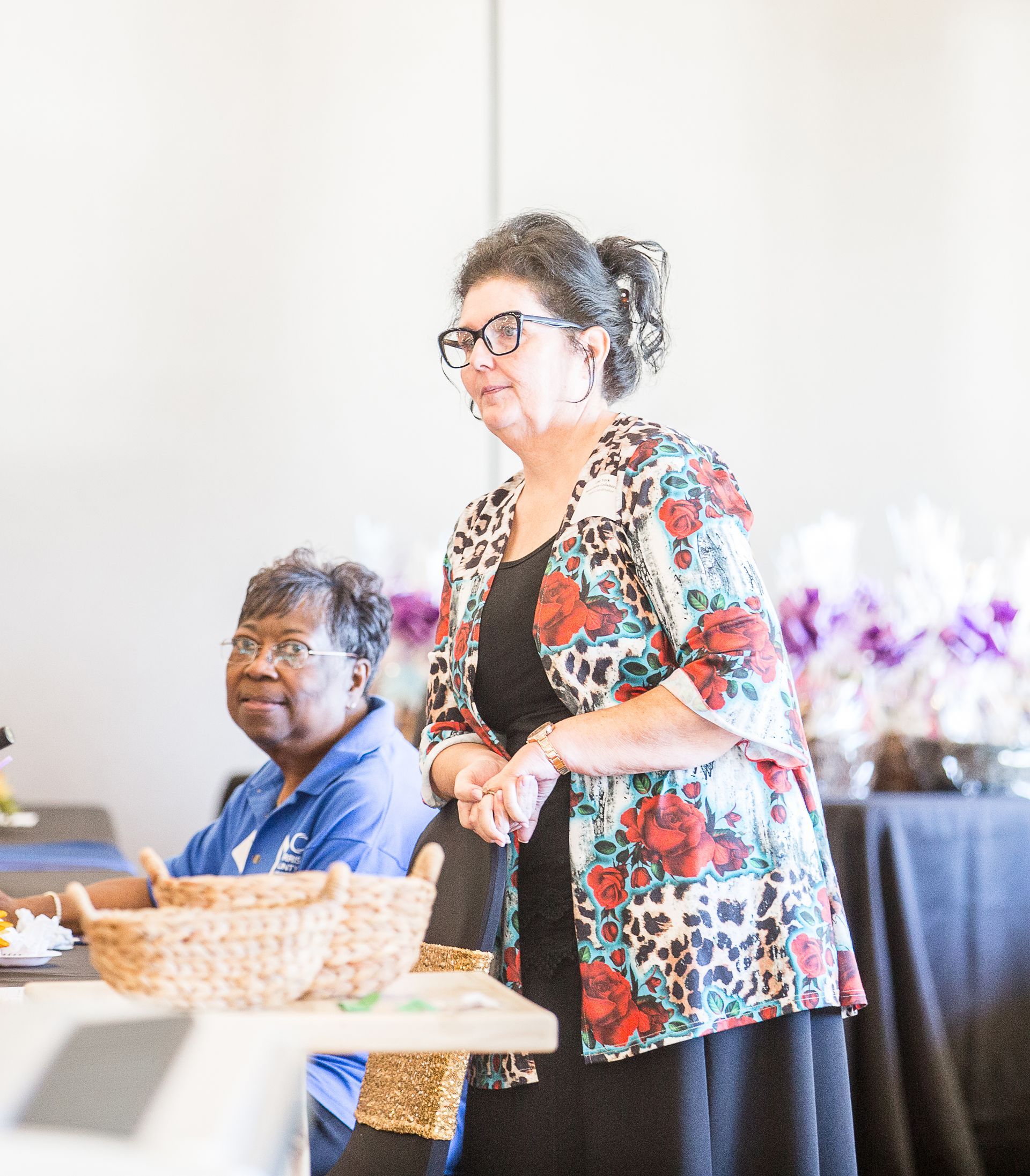 A woman in a floral jacket is standing in front of a table.