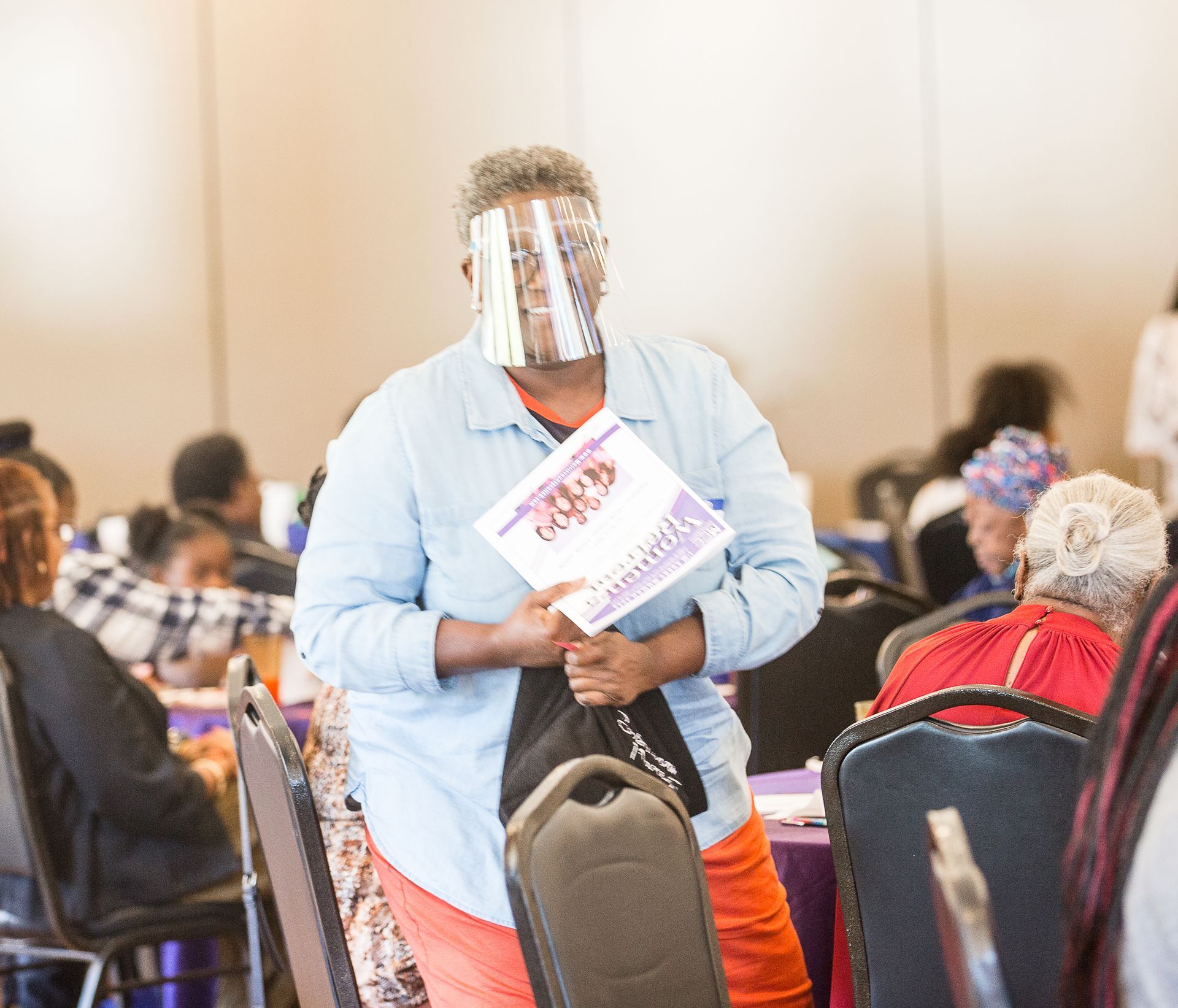 A woman wearing a face shield is holding a piece of paper.