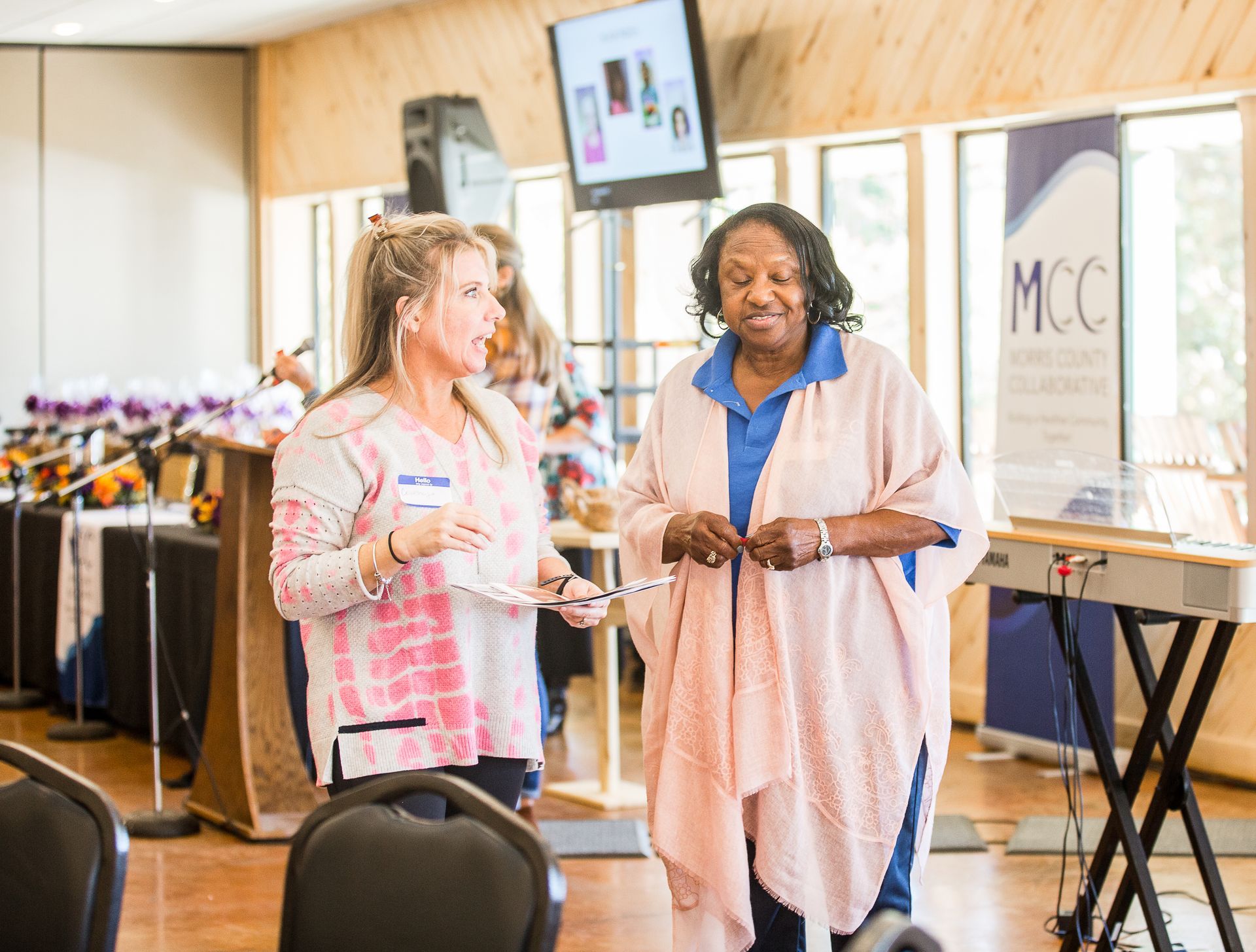 Two women are standing next to each other in a room talking.