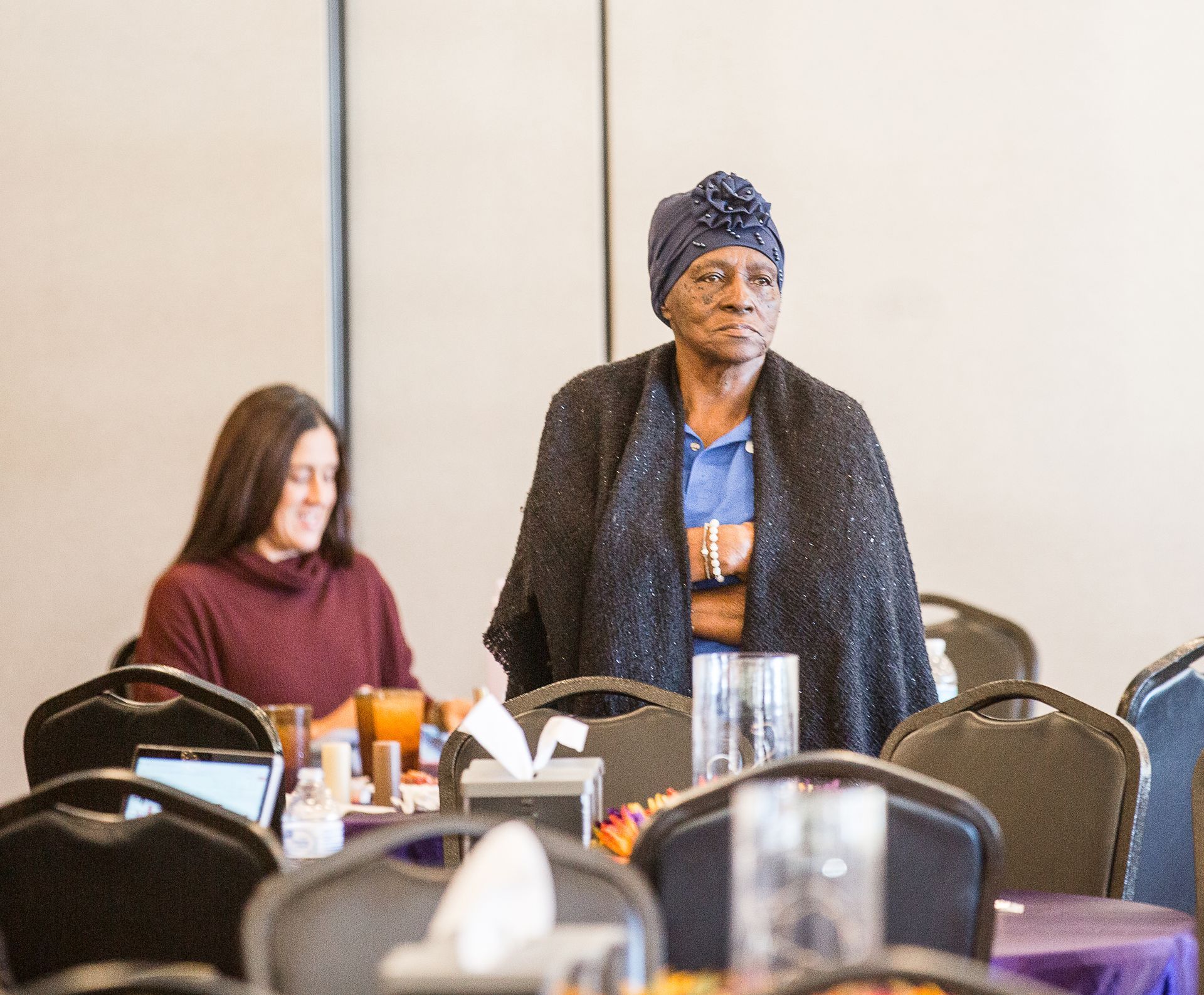 A woman in a turban is standing in a room with tables and chairs.