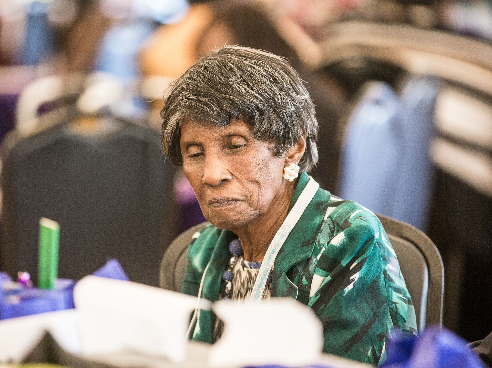 An elderly woman is sitting at a table reading a book.