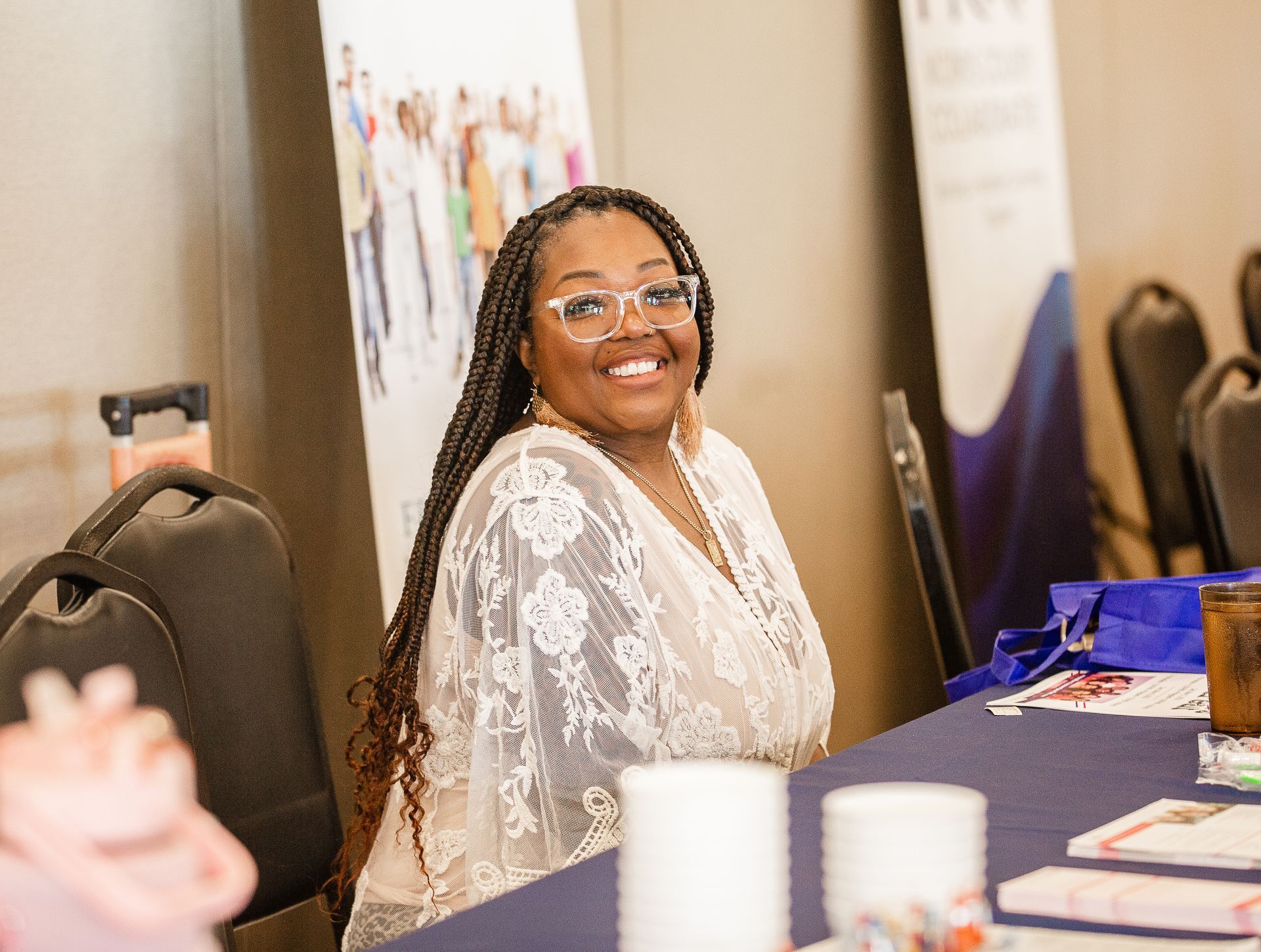 A woman wearing glasses is sitting at a table and smiling.