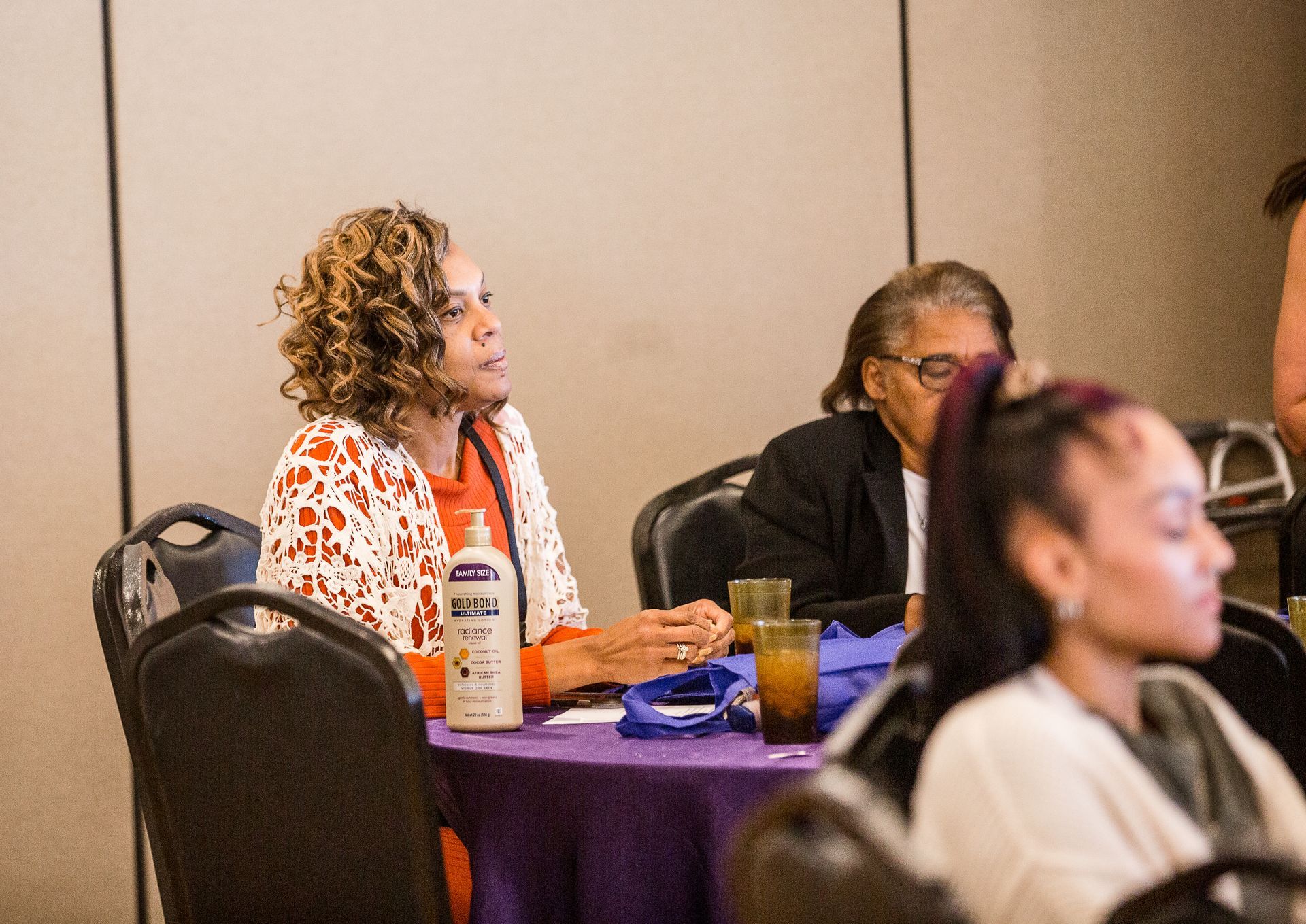 A woman is sitting at a table with a bottle of lotion on it.
