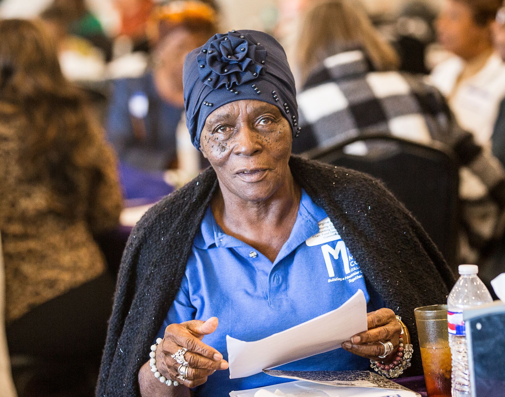 A woman in a blue shirt is sitting at a table holding a piece of paper.