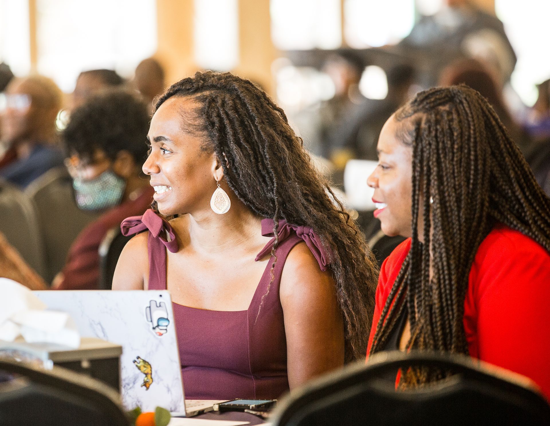 Two women with dreadlocks are sitting in front of a laptop computer.