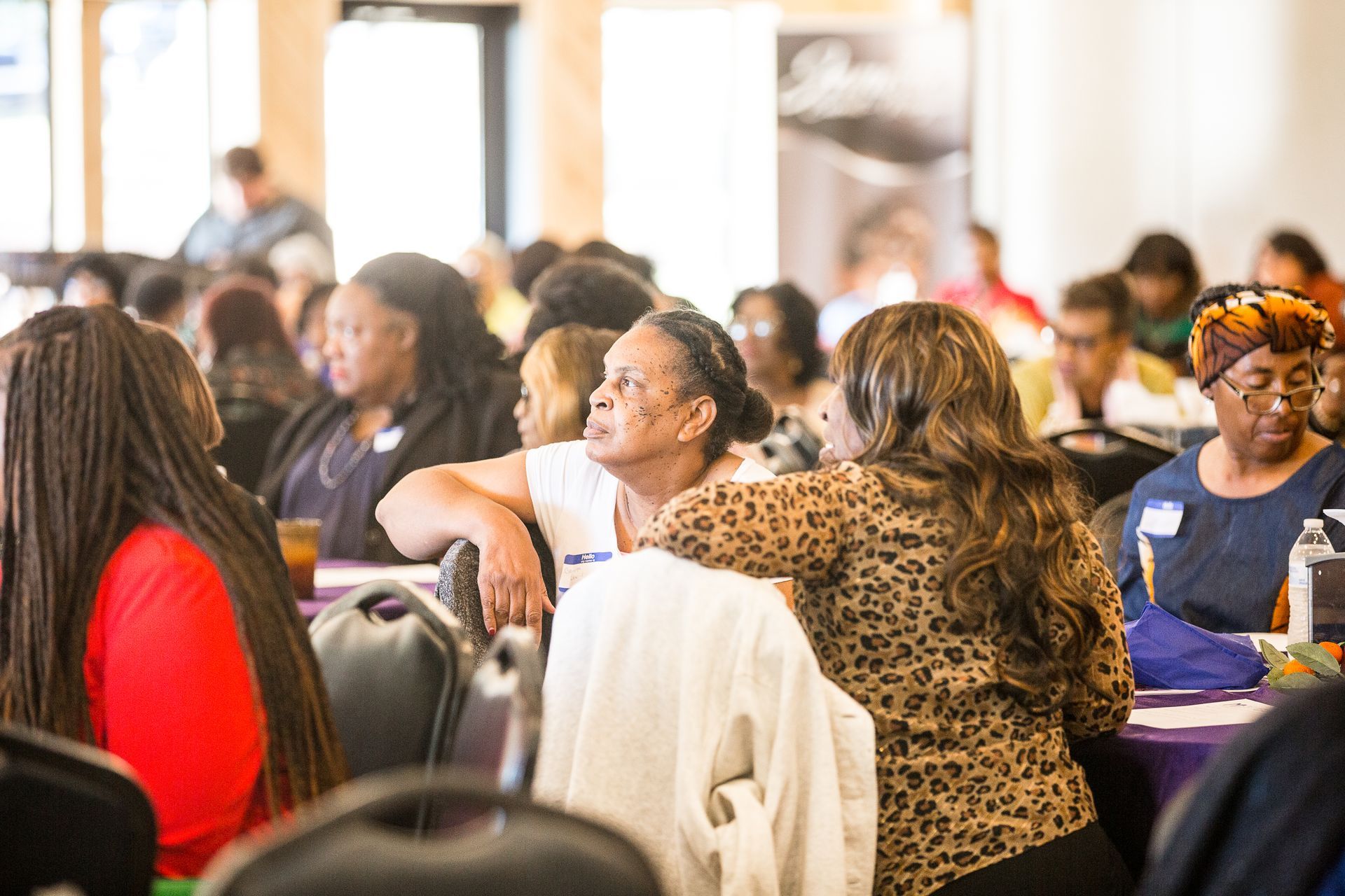 A group of women are sitting at tables in a room talking to each other.
