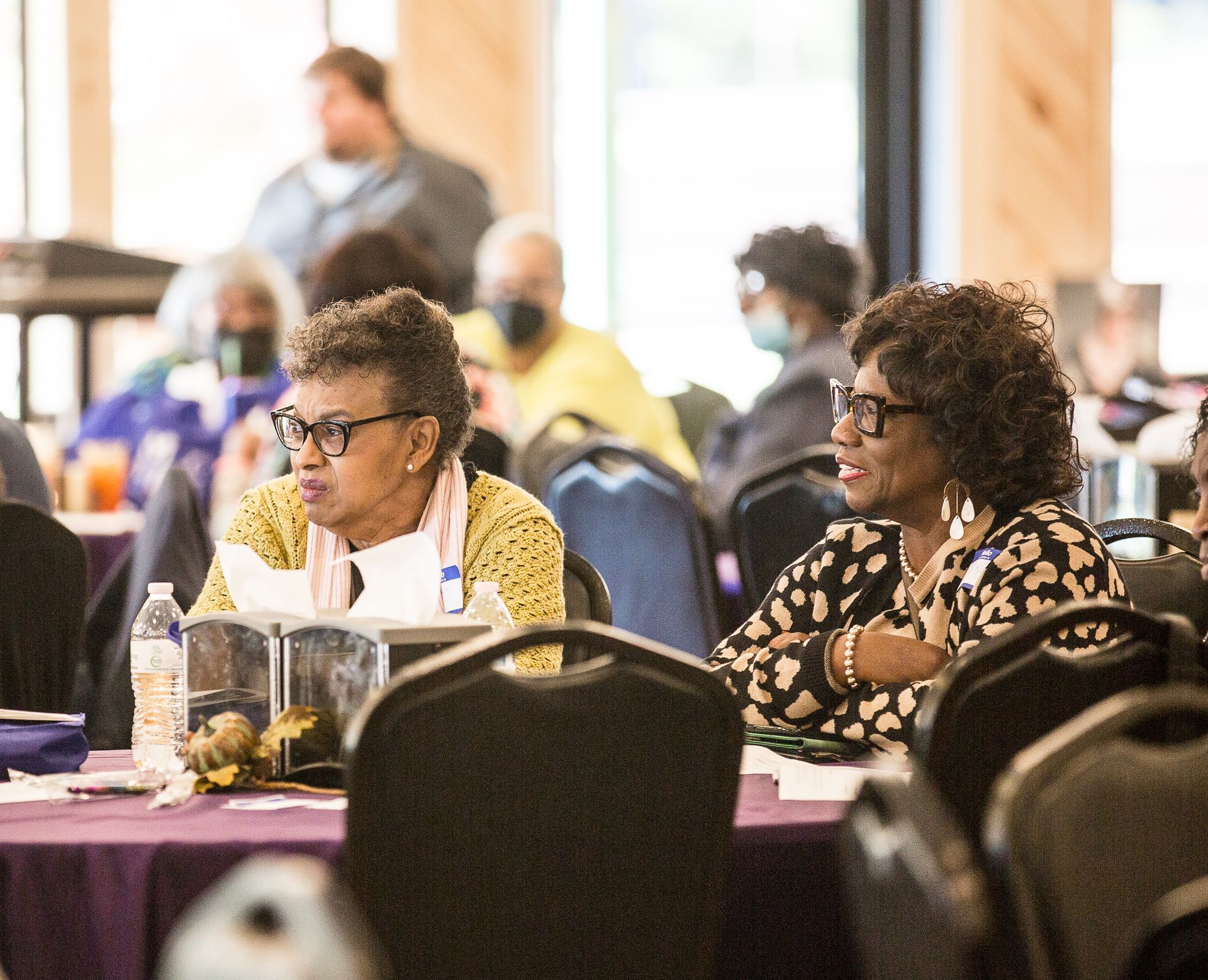 Two women are sitting at a table in a conference room.