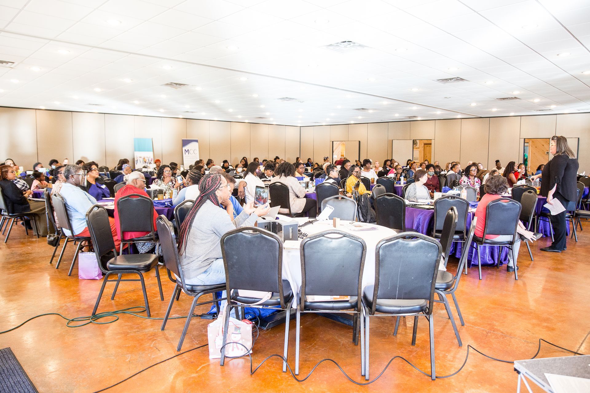 A large room filled with people sitting at tables and chairs.