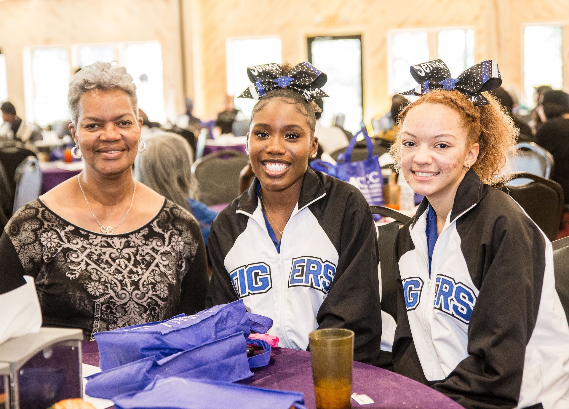 A group of cheerleaders are sitting at a table with a woman.