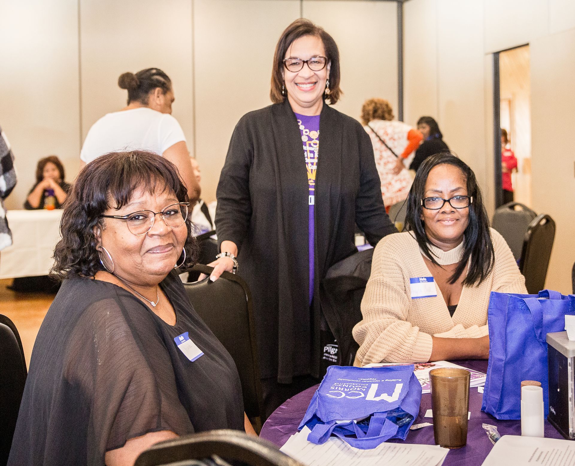 Three women are posing for a picture while sitting at a table.