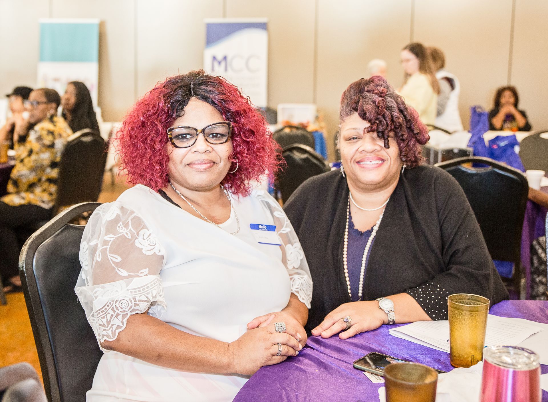 Two women are posing for a picture while sitting at a table.
