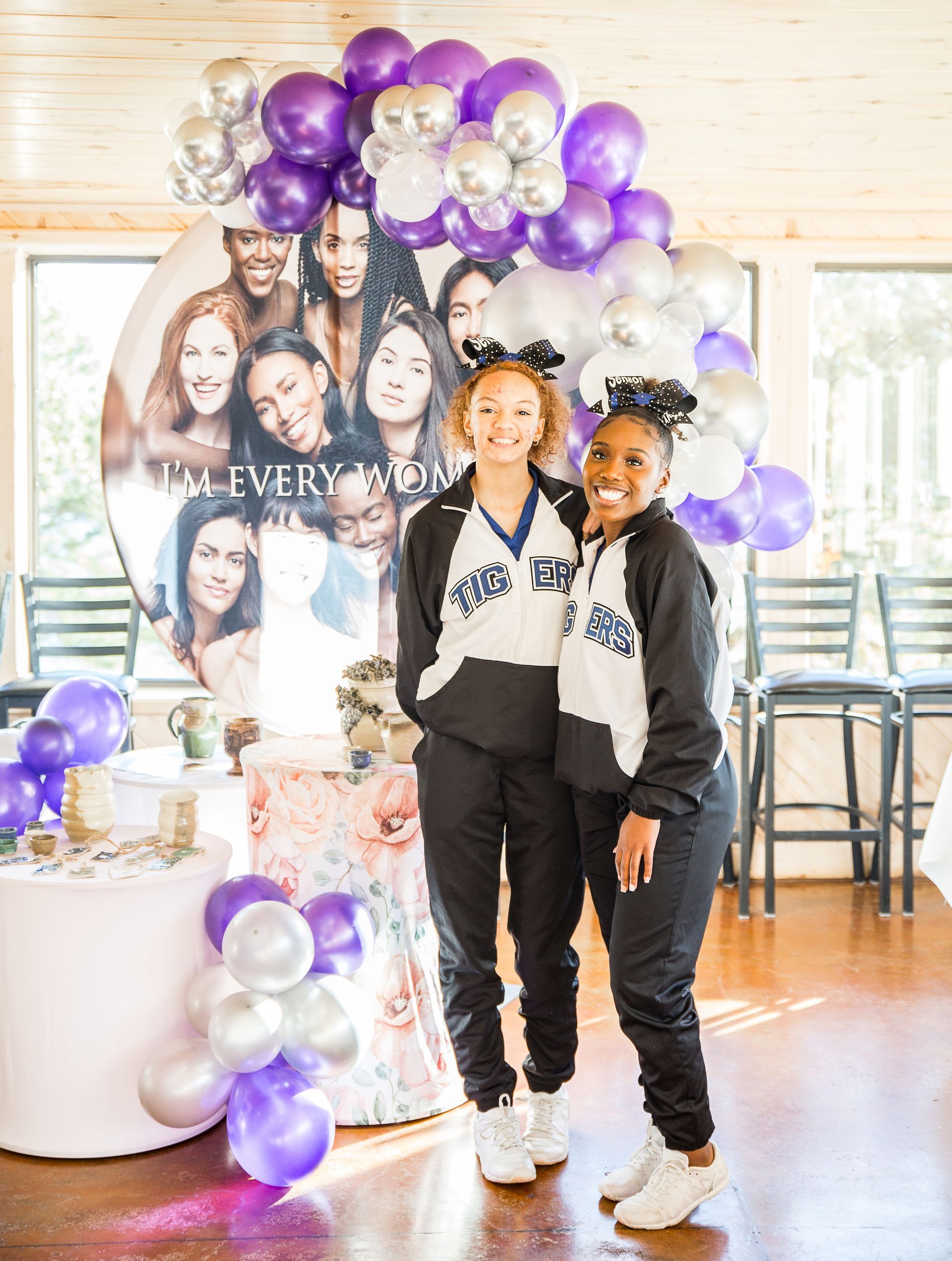 Two cheerleaders are posing for a picture in front of balloons.