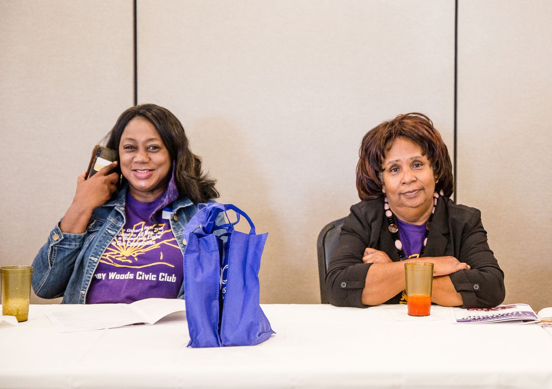 Two women are sitting at a table with their arms crossed.