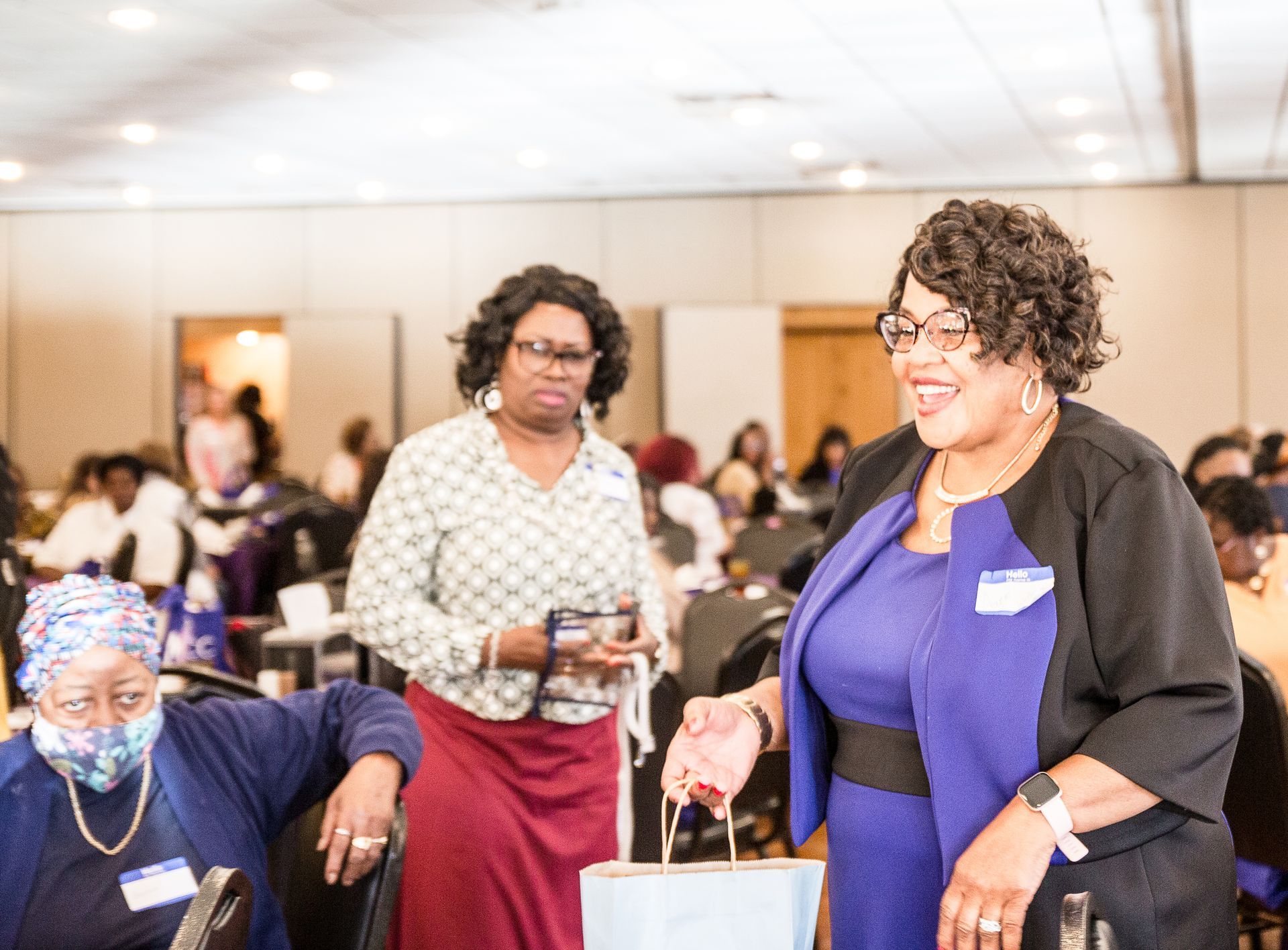 A group of women are standing in a room holding bags and smiling.