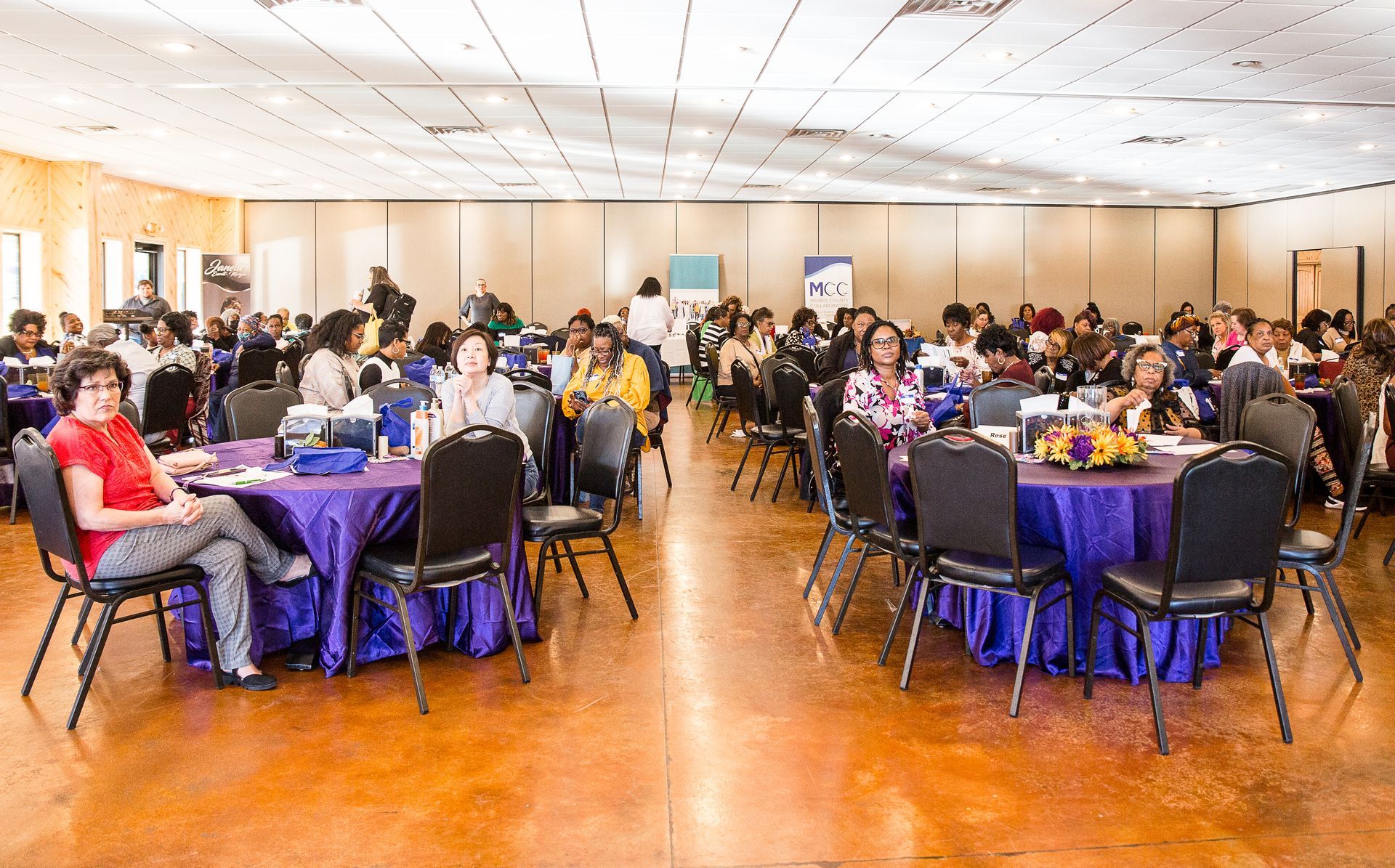 A large room filled with tables and chairs and people sitting at tables.