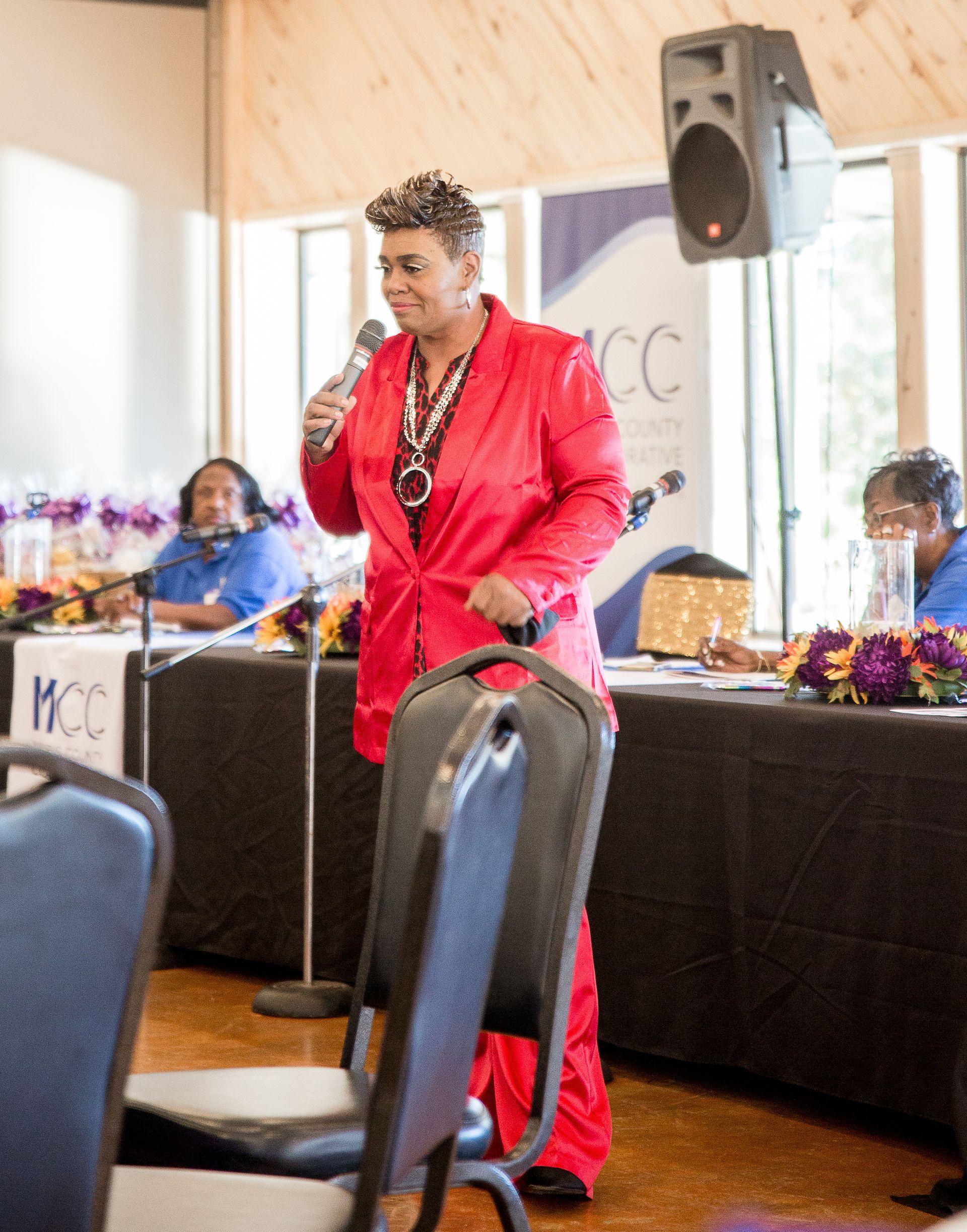 A woman in a red suit is speaking into a microphone