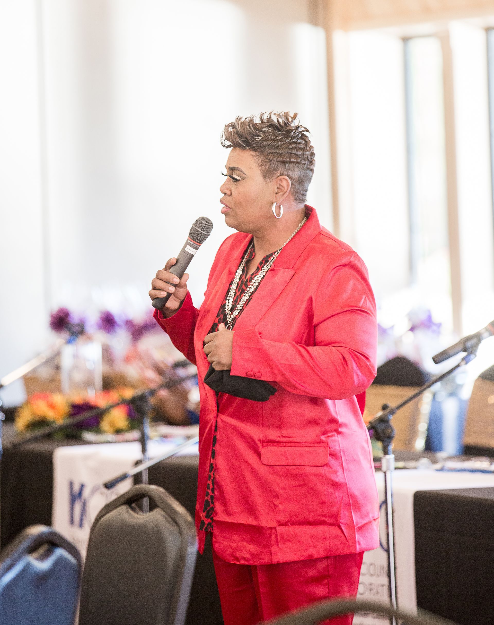 A woman in a red jacket is speaking into a microphone