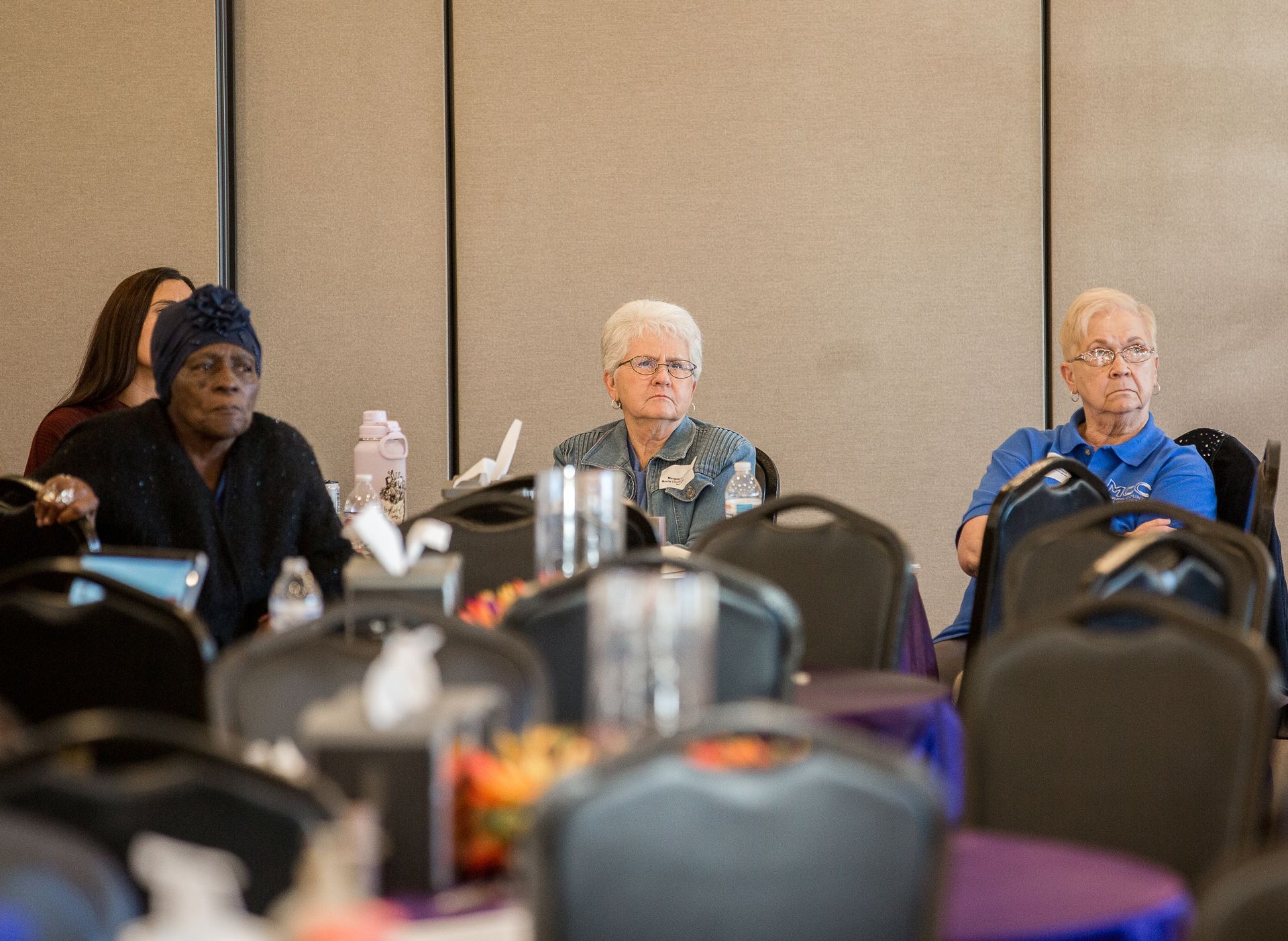 A group of older women are sitting at tables in a conference room.