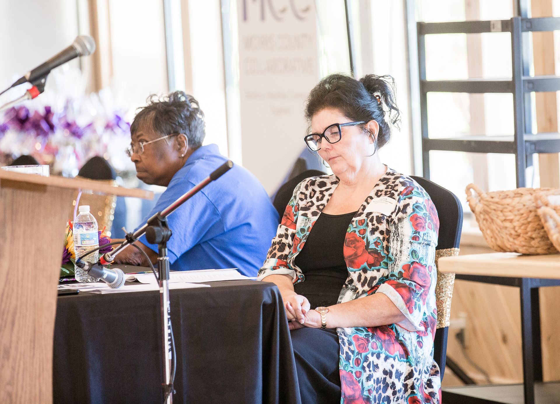 Two women are sitting at a table with microphones in front of them.