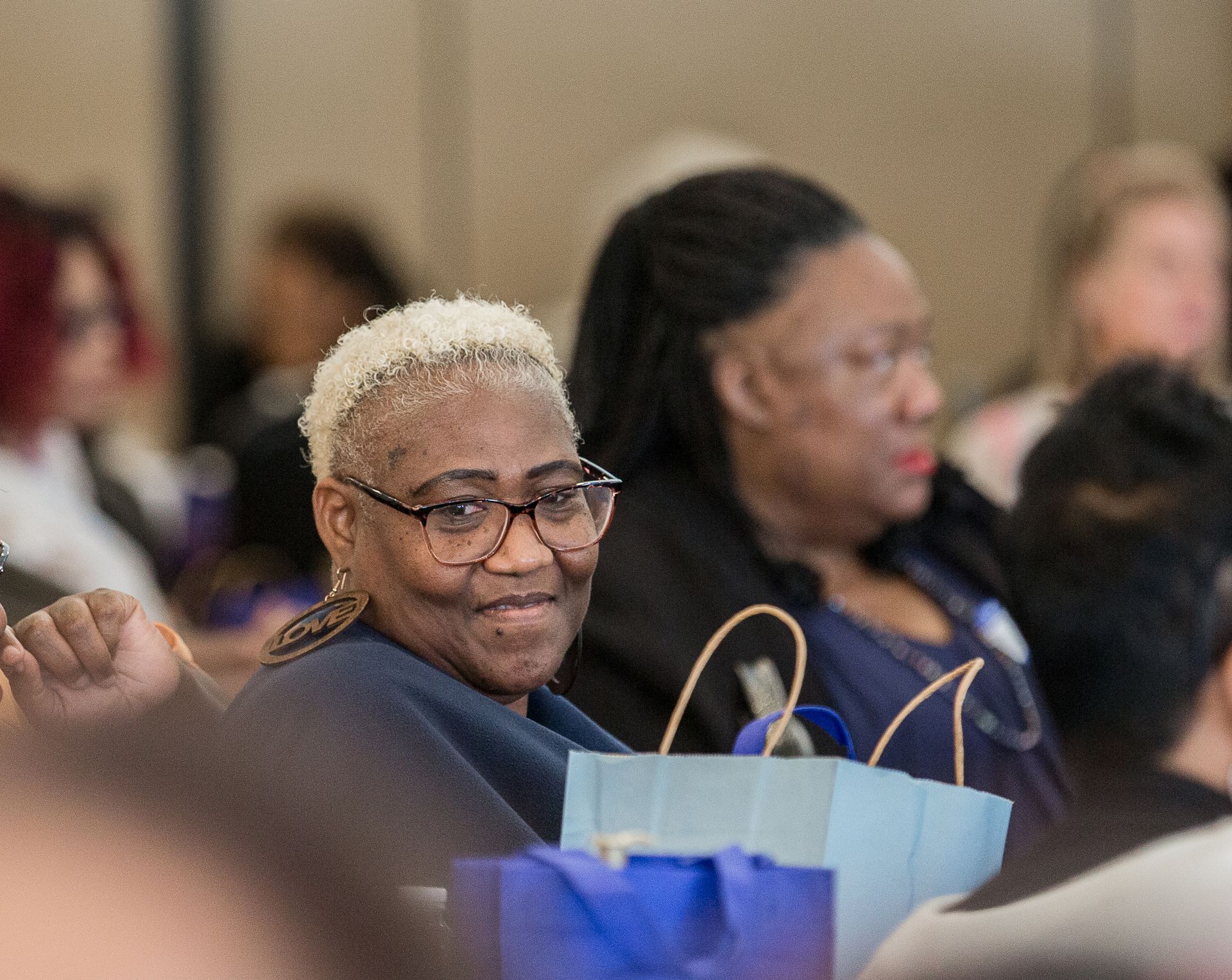 A woman wearing glasses is smiling while holding a blue bag.