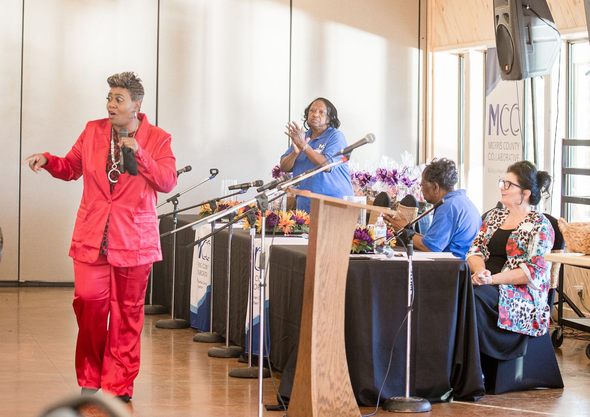A woman in a red suit is standing in front of a podium talking into a microphone.