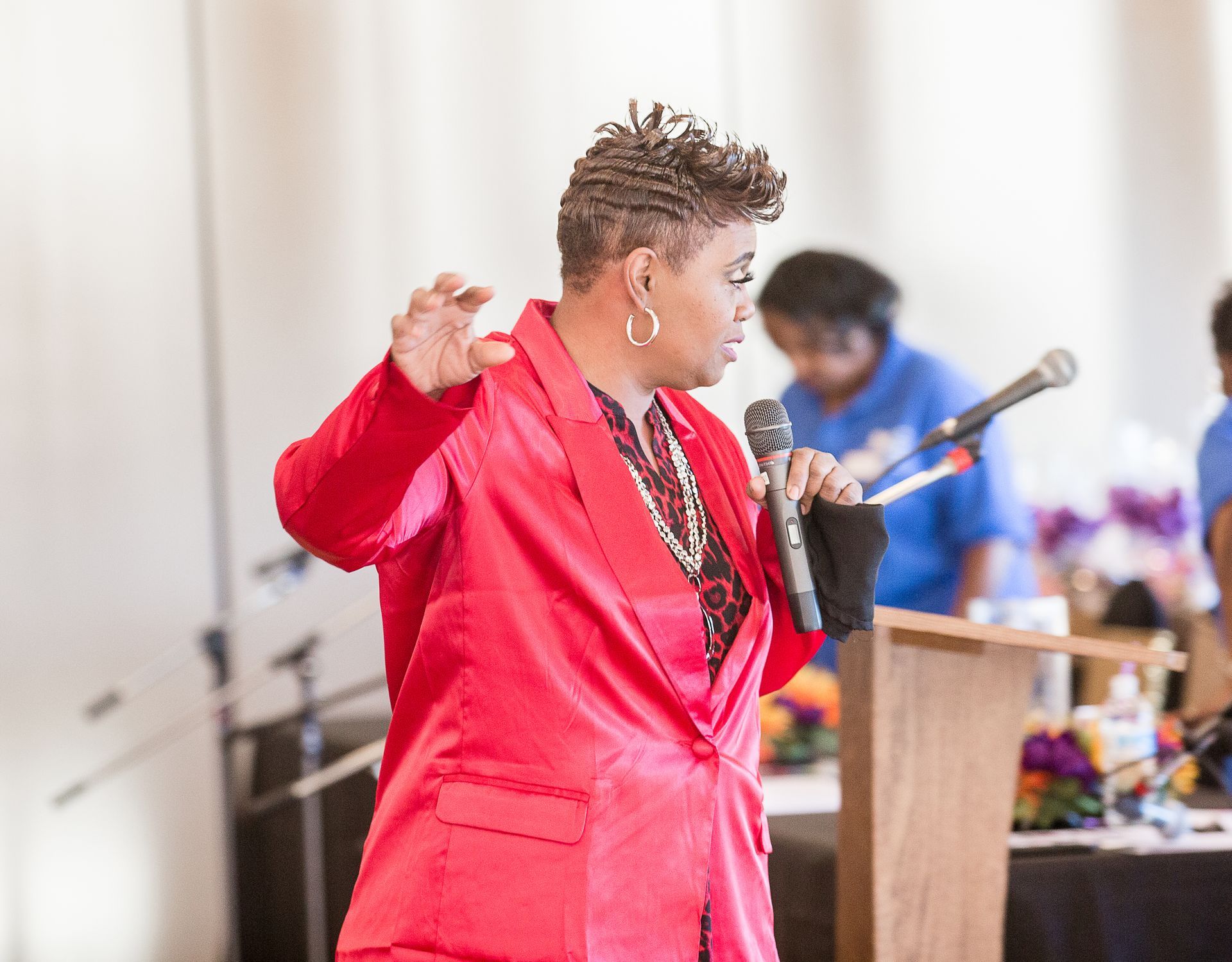 A woman in a red jacket is singing into a microphone.