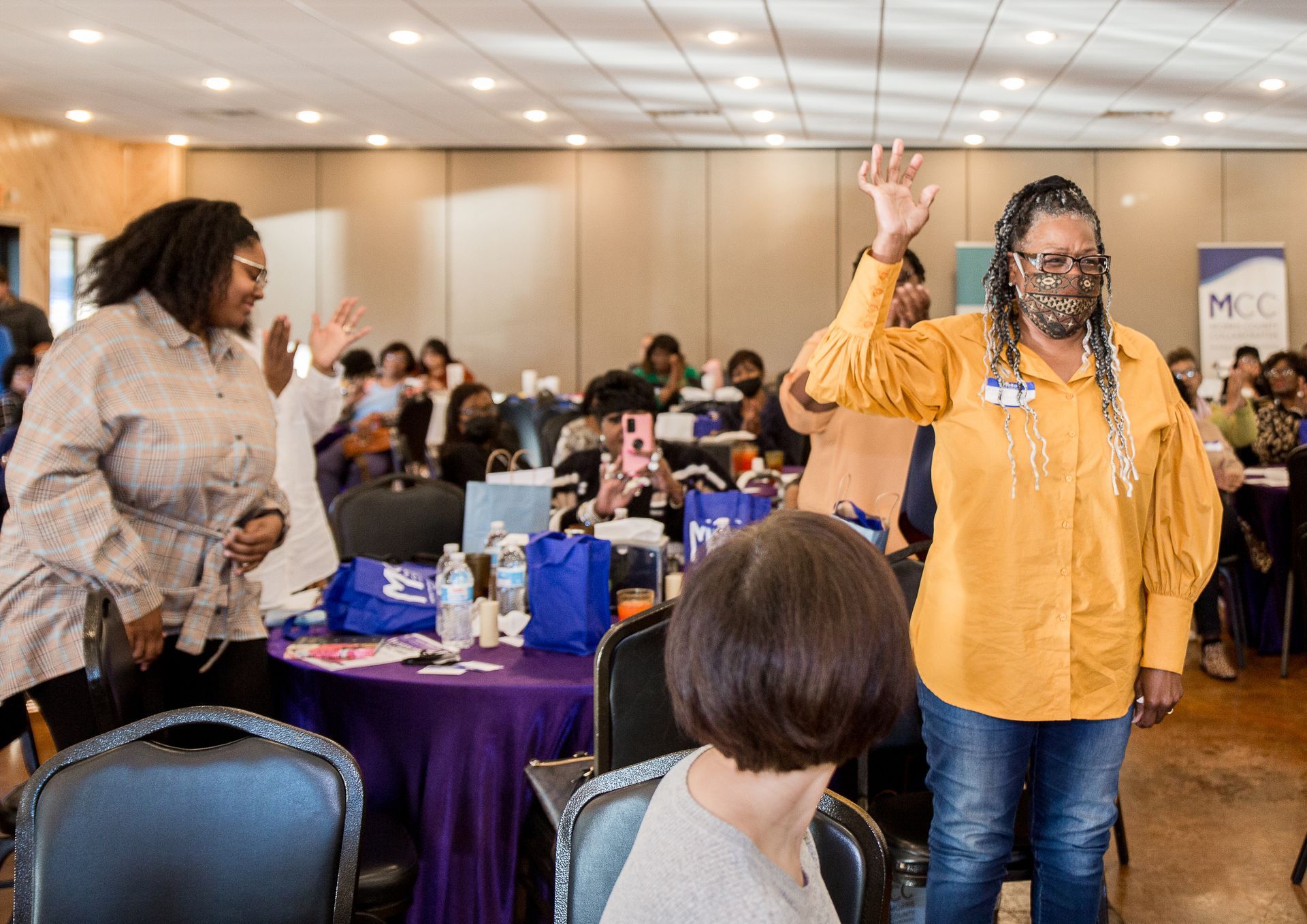 A group of women are dancing in a room with tables and chairs.