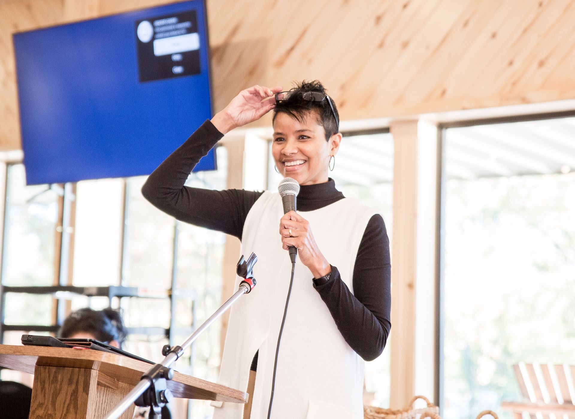 A woman is standing at a podium holding a microphone and smiling.