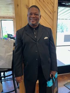 A man in a suit is standing in front of a wooden wall and smiling.