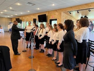 A man is leading a choir of women in a room.