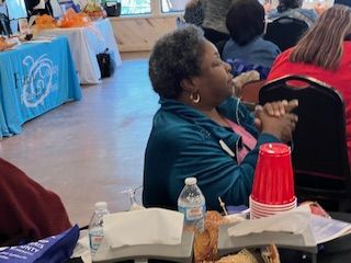A woman is sitting at a table with her hands folded in prayer.