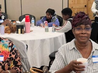 A woman is sitting at a table holding a cup of coffee.