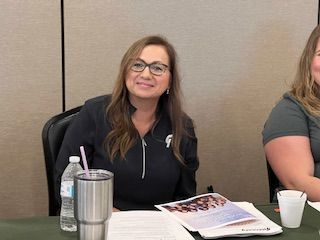 Two women are sitting at a table with a cup of coffee and a bottle of water.