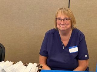 A woman wearing glasses and a name tag is sitting at a table.