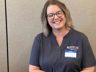 A woman wearing glasses and a name tag is smiling.