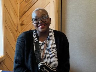 A woman wearing glasses and a striped shirt is smiling while sitting at a table.