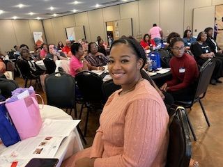 A woman is sitting at a table in a room with other people.