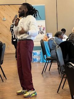 A man is standing in front of a group of people holding a microphone.