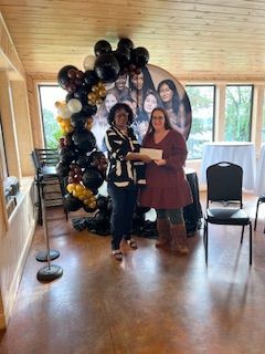 Two women are standing next to each other in a room with balloons in the background.