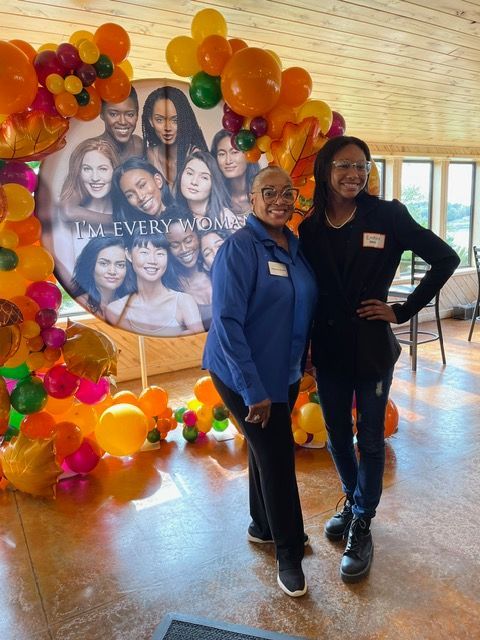 Two women are posing for a picture in front of balloons.