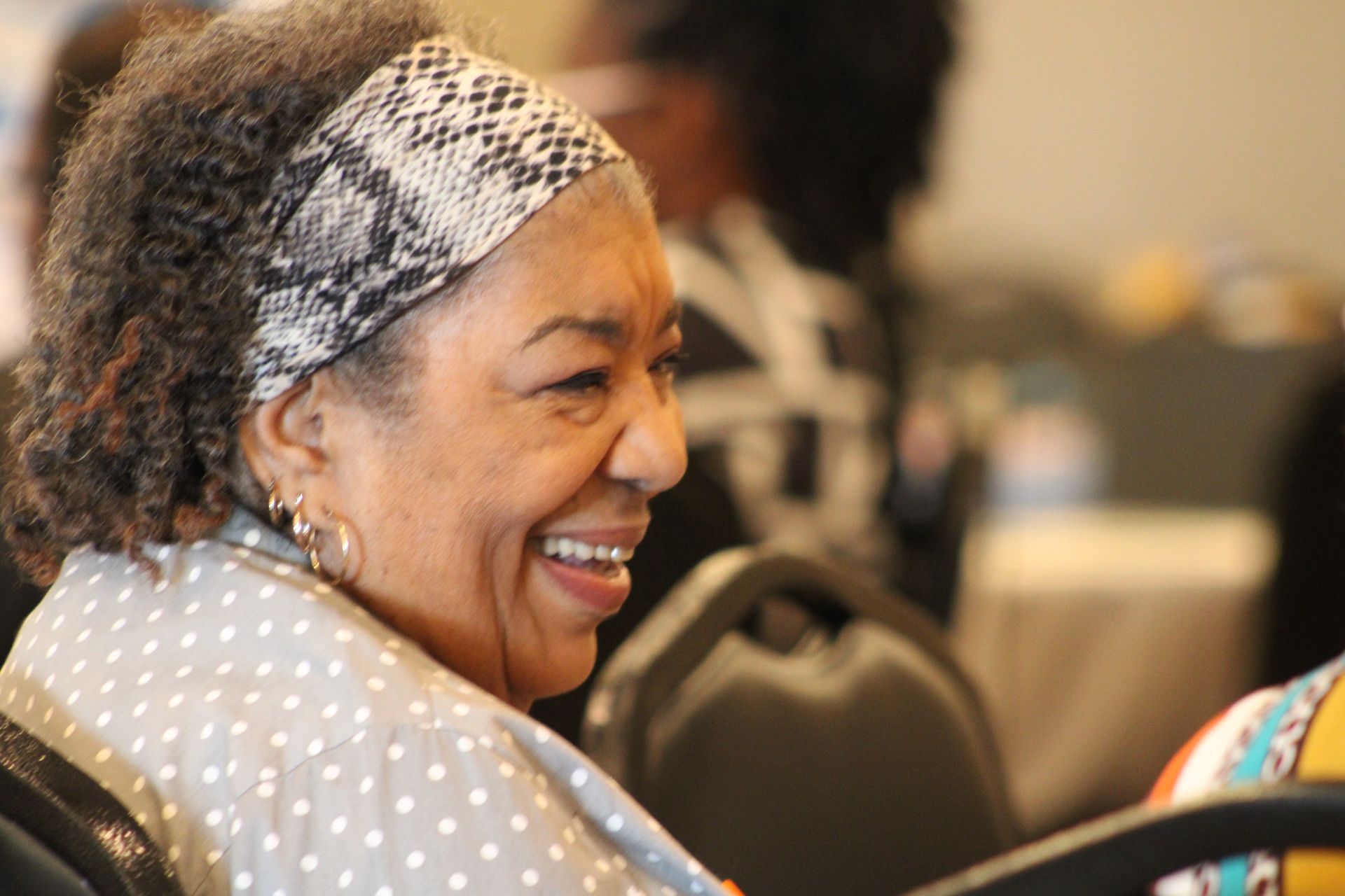 A woman wearing a headband is smiling while sitting in a chair.