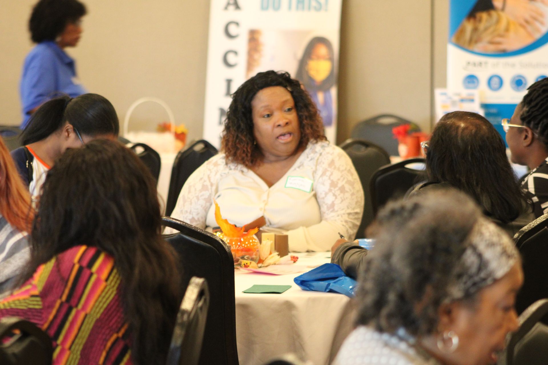 A woman is sitting at a table in front of a sign that says do trust