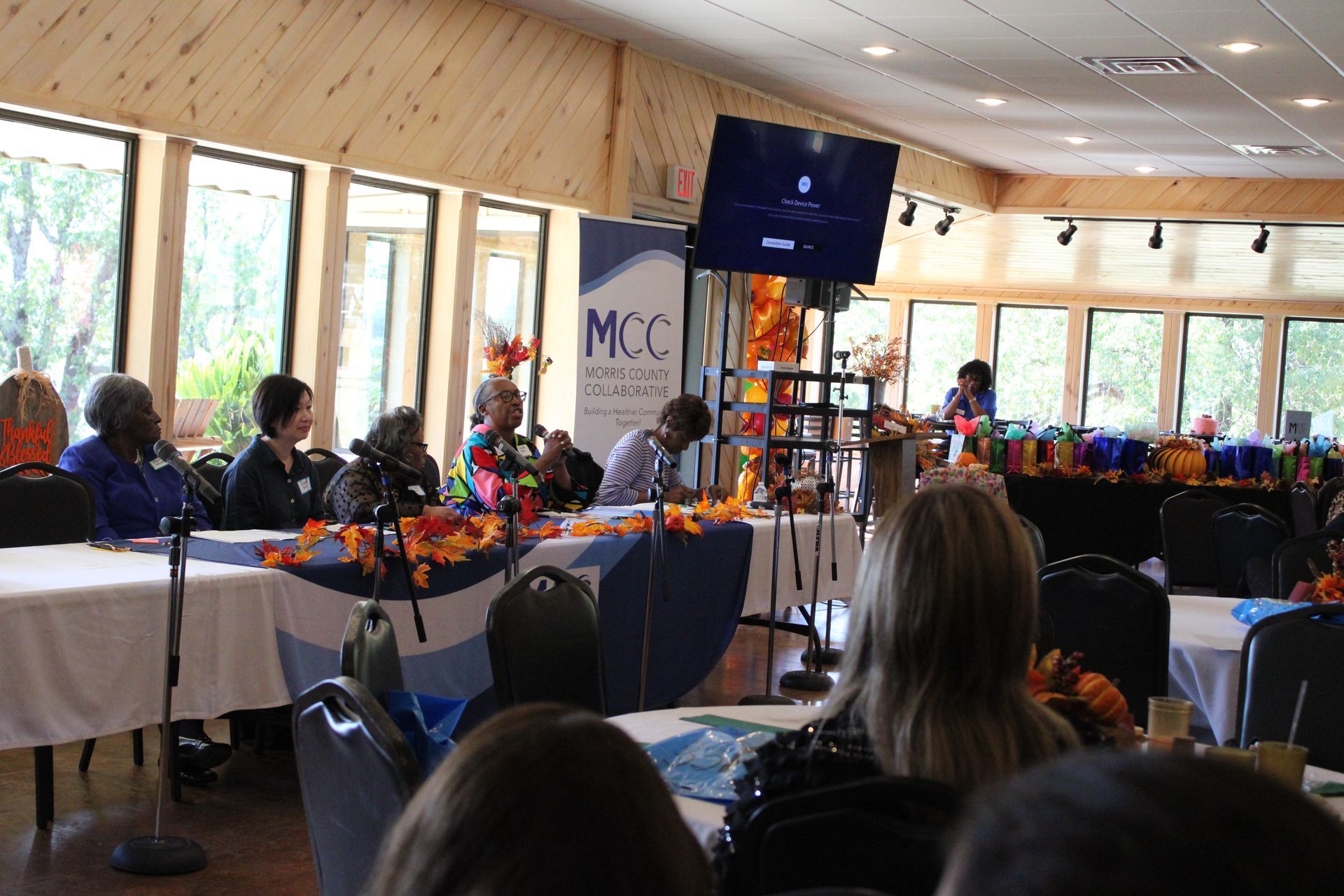 A group of people are sitting at tables in a room with a sign that says mcc