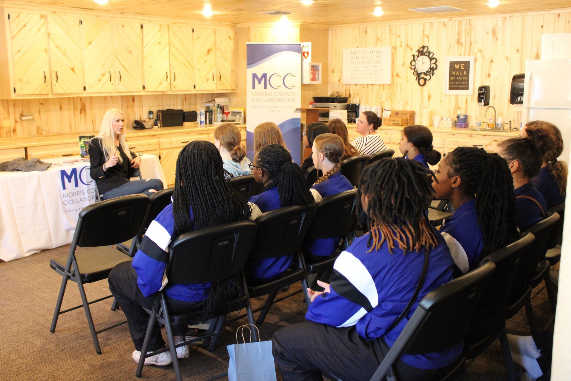 A group of people are sitting in chairs in front of a mcc sign.